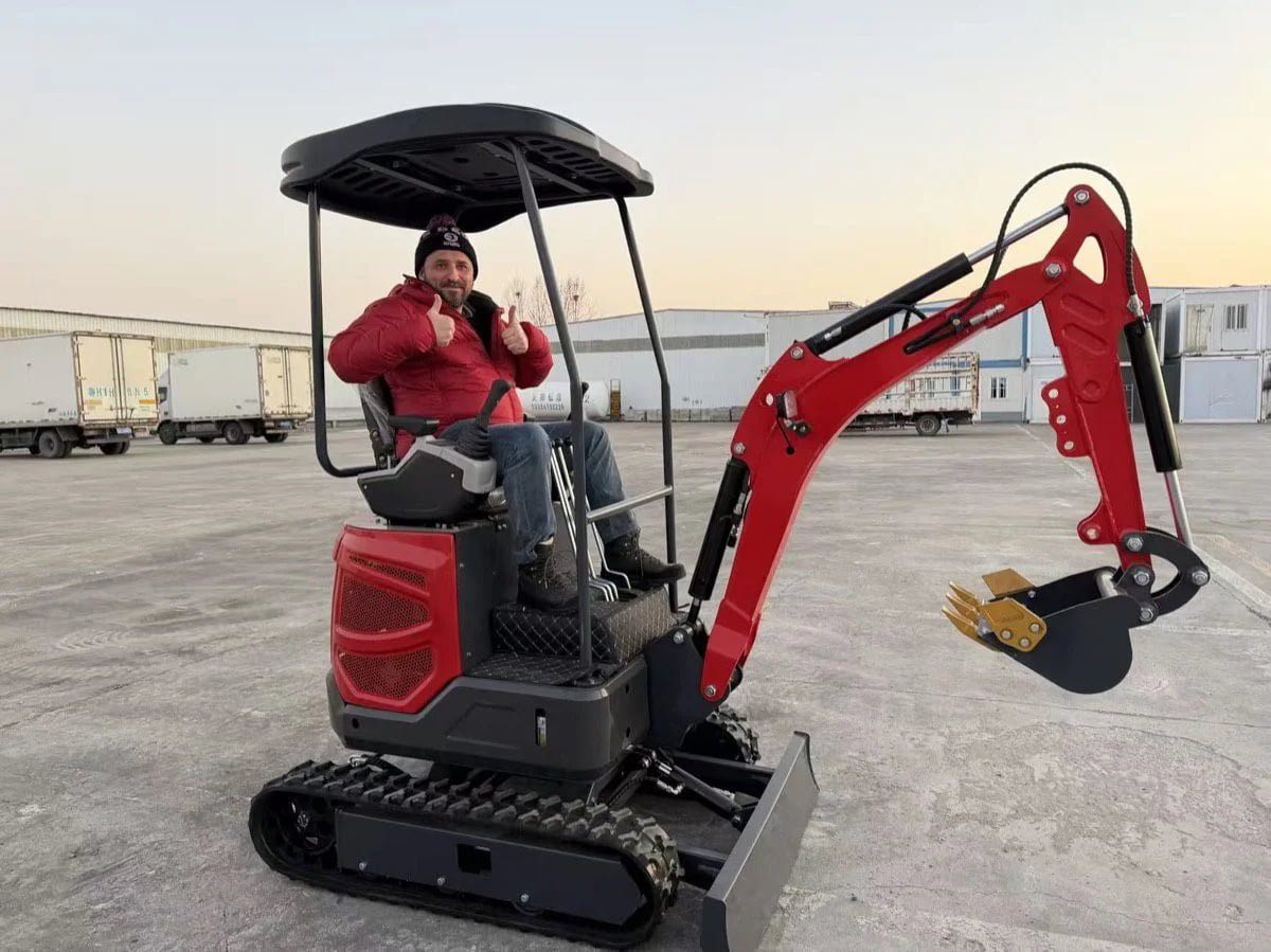 Red compact excavator with operator at an equipment yard
